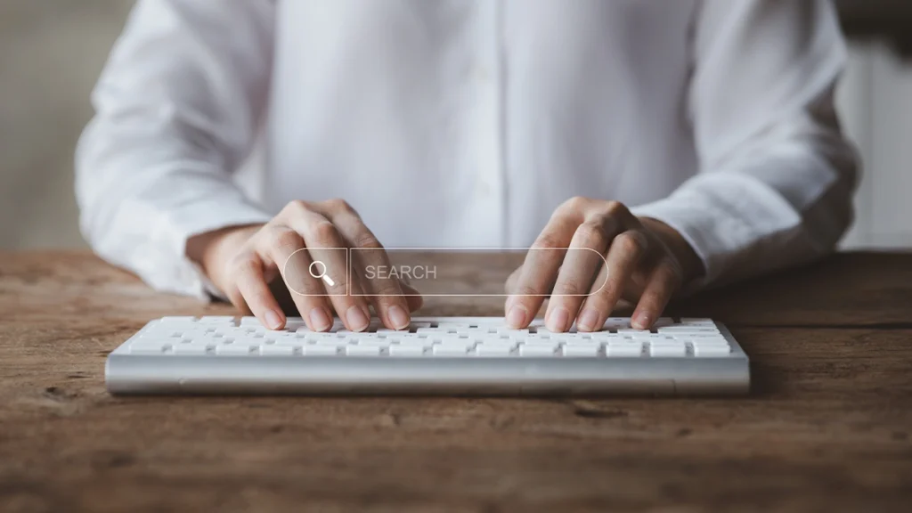 Male wearing a white shirt typing on a keyboard with a holographic search bar