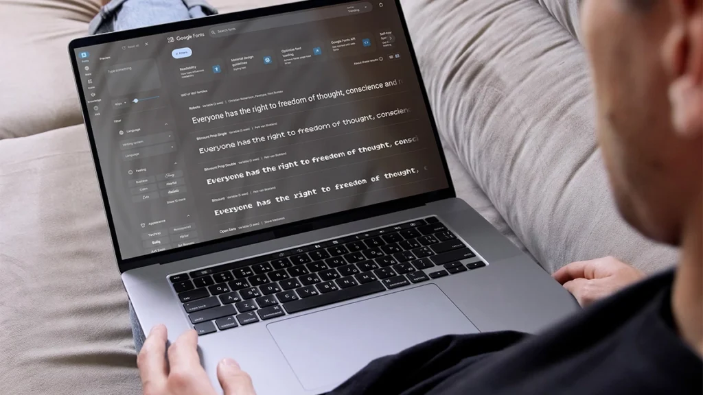 Man sitting on a sofa, looking at Google fonts on laptop