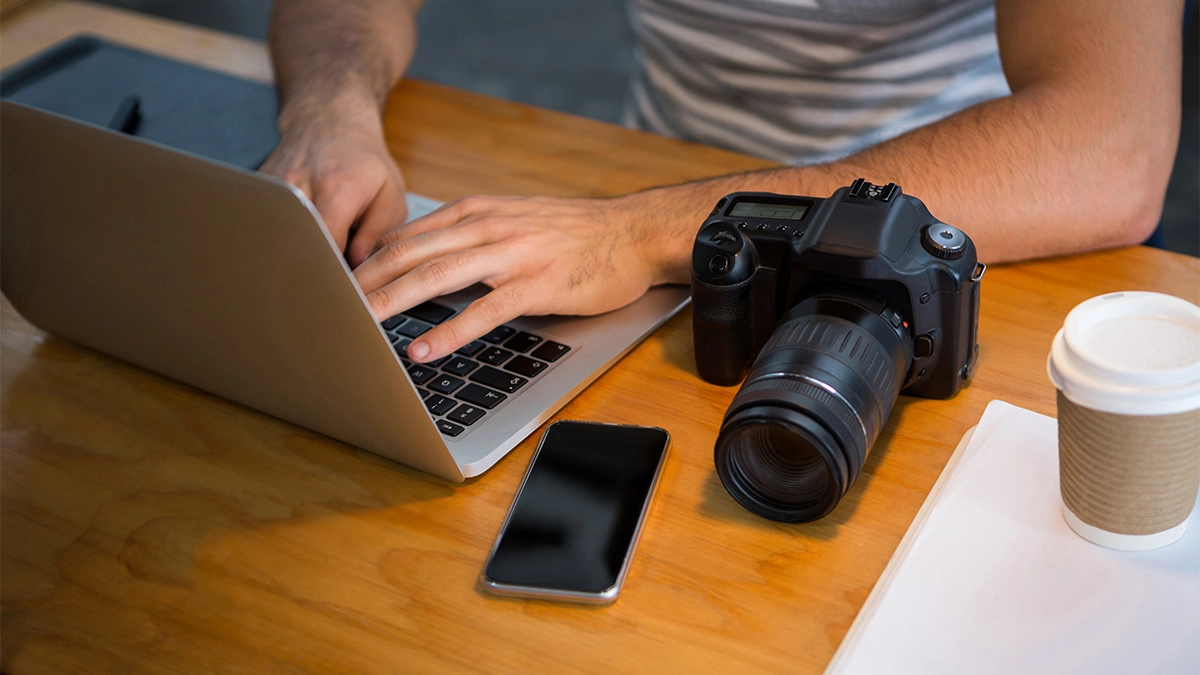 Man using a laptop with camera sitting next to him on the table