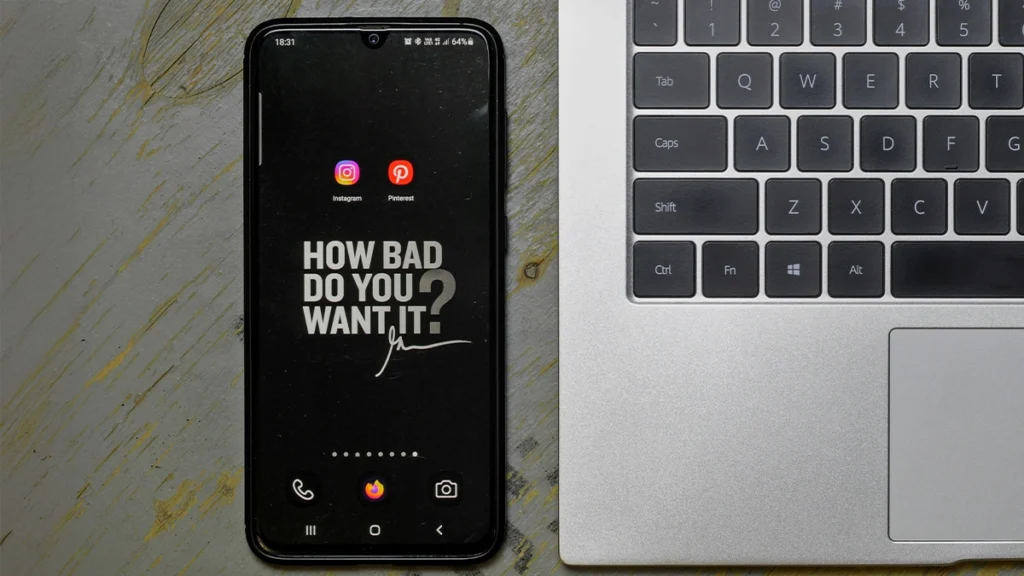 Phone with social media icons next to a laptop.