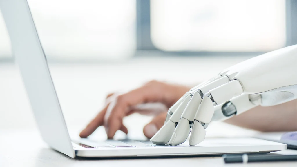 Human and robot hands typing on keyboard