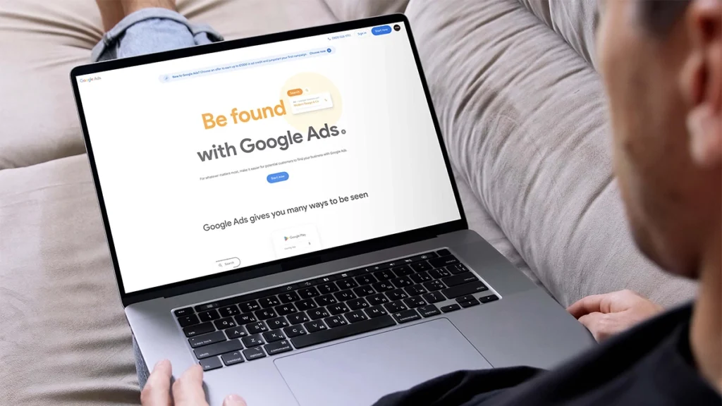 Man sitting on couch looking at Google Ads landing page on laptop