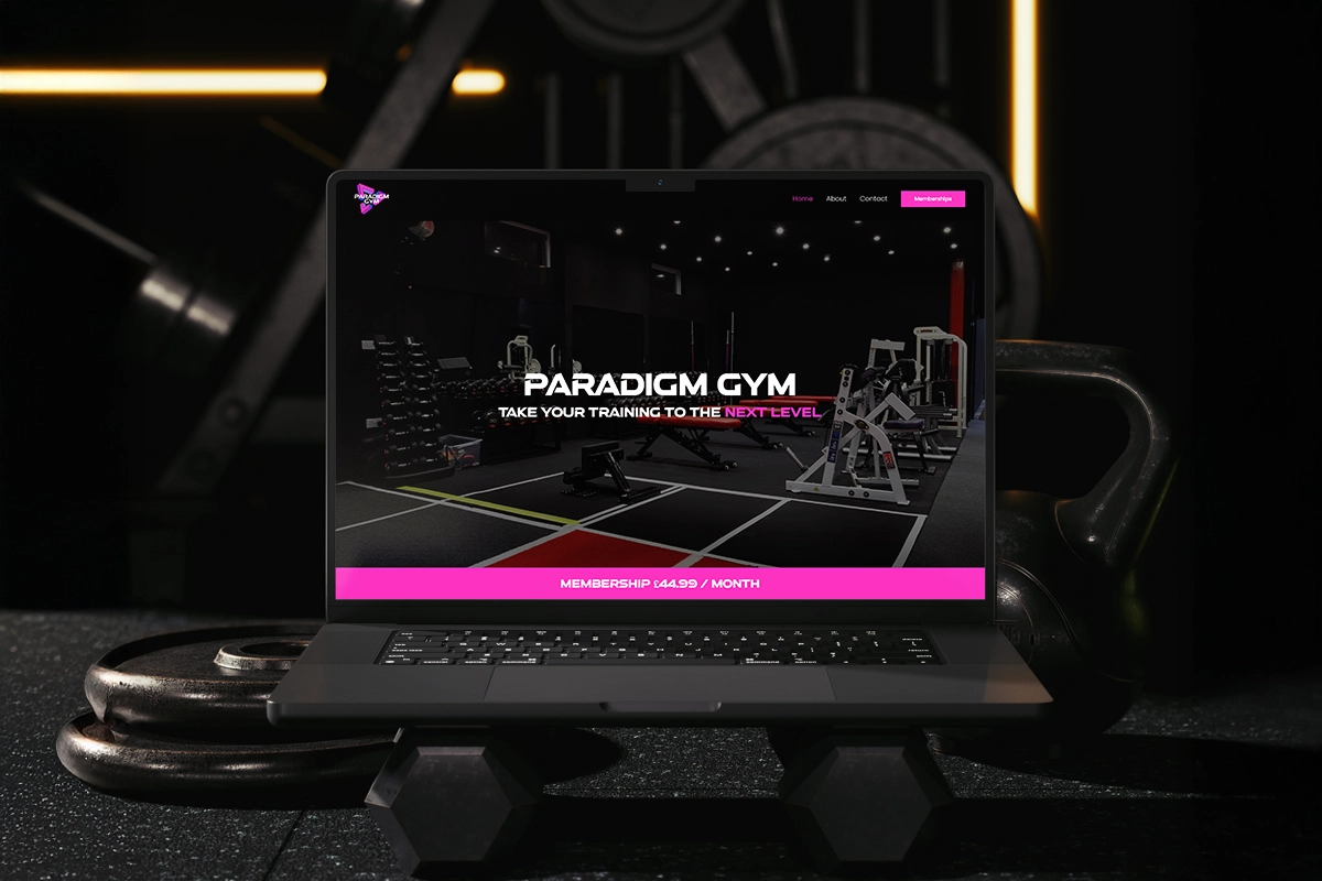 Laptop sitting on dumbbells in a gym with the Paradigm Gym website on screen