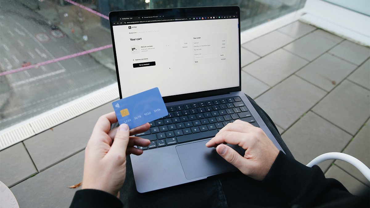 Man holding bank card and placing e-commerce order on laptop
