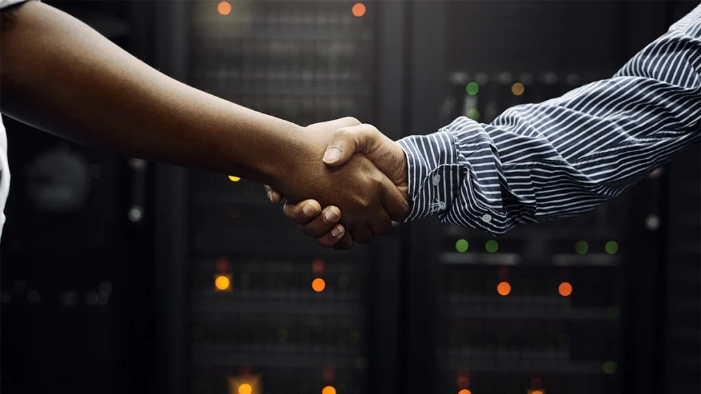 Two hands shaking in front of website hosting server