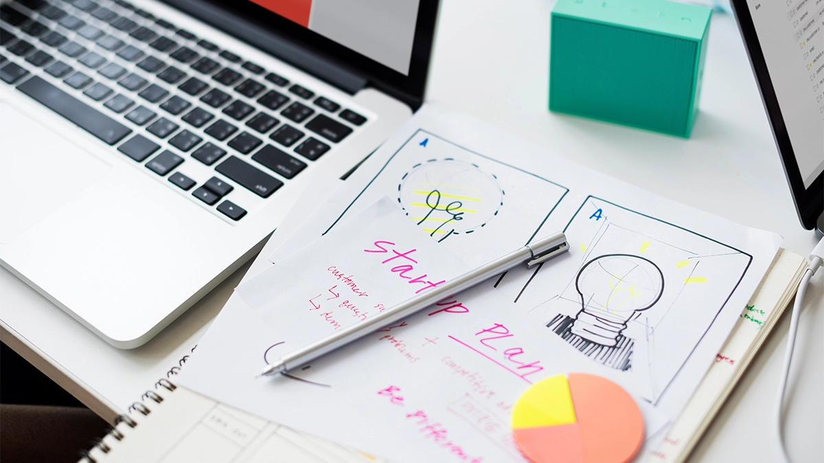 Laptop and notepad with startup notes on desk