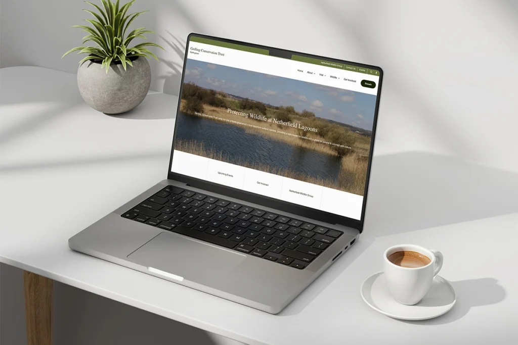 Laptop with Gedling Conservation Trust website, alongside espresso mug and pot plant